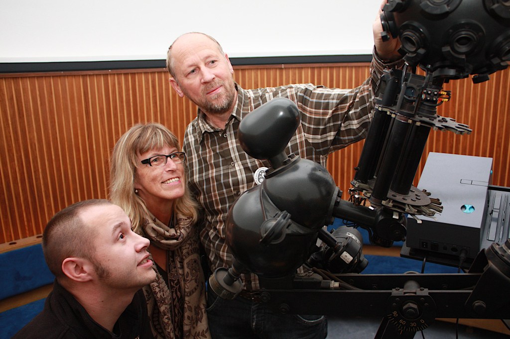 Menschen vor einem optischen Projektor im Planetarium in Bremerhaven, die auf die Technik zeigen und dabei interessiert miteinander sprechen.