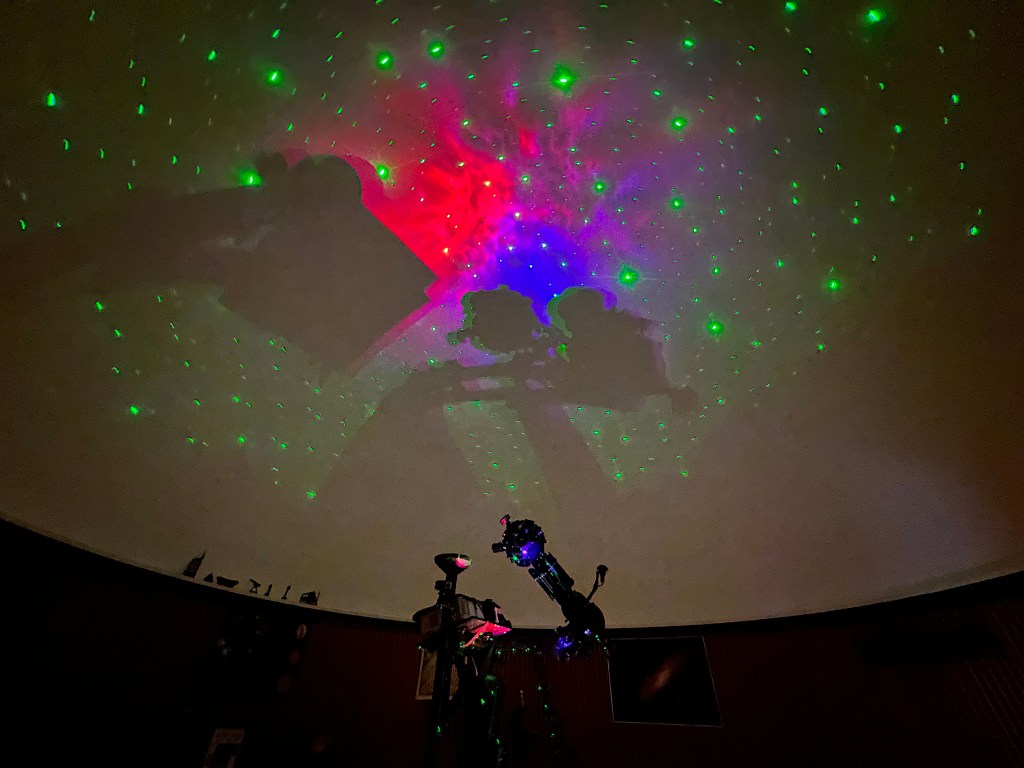 Lichtprojektionen in einem Planetarium mit grünen und roten Sternen, die an die Kuppeldecke geworfen werden.