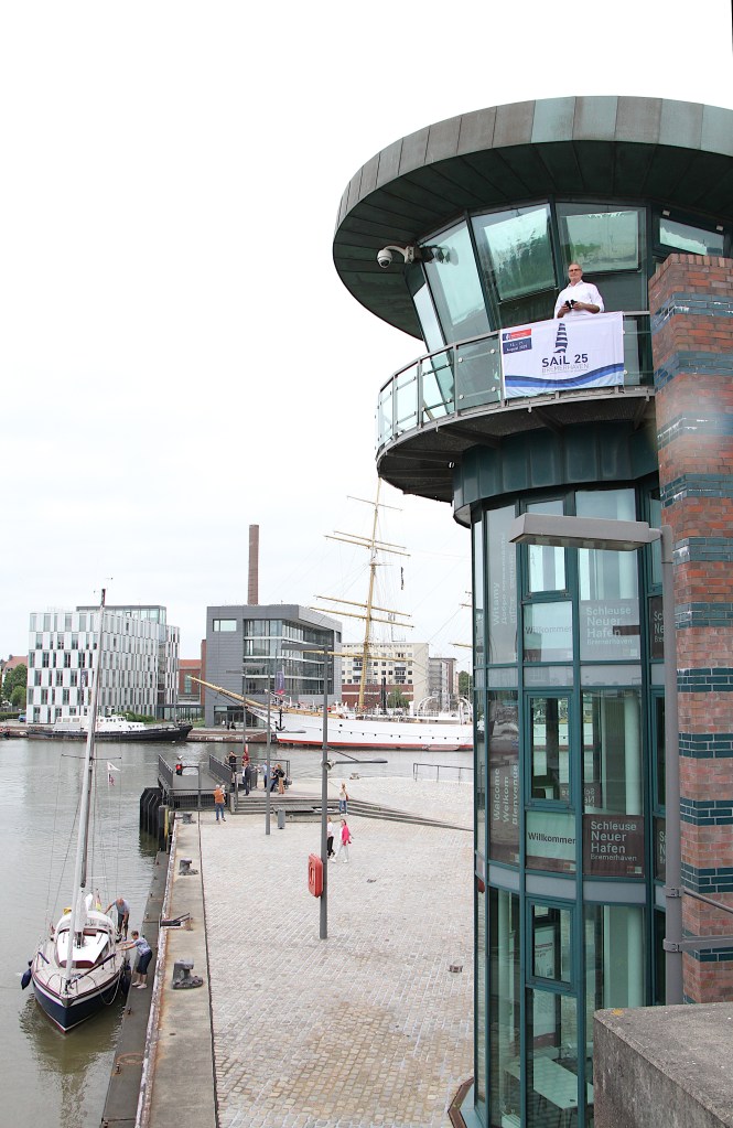 Ausblick vom Kontrollturm der Schleuse am Neuen Hafen, mit einem Schleusenwärter, einem Schiff im Hintergrund und Besuchern an der Uferpromenade.