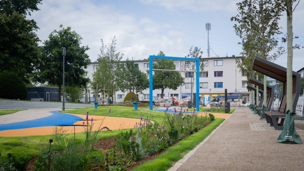 Neugestalteter kirchPARK mit Spielplatz, blauen Spielgeräten und grüner Landschaftsgestaltung in der Innenstadt.