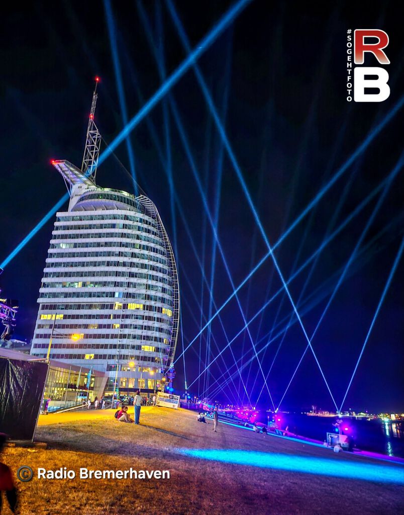 Nachtaufnahme des Windjammer-Festivals in Bremerhaven mit strahlenden Lichtern, die vom Gebäude in den Himmel leuchten.