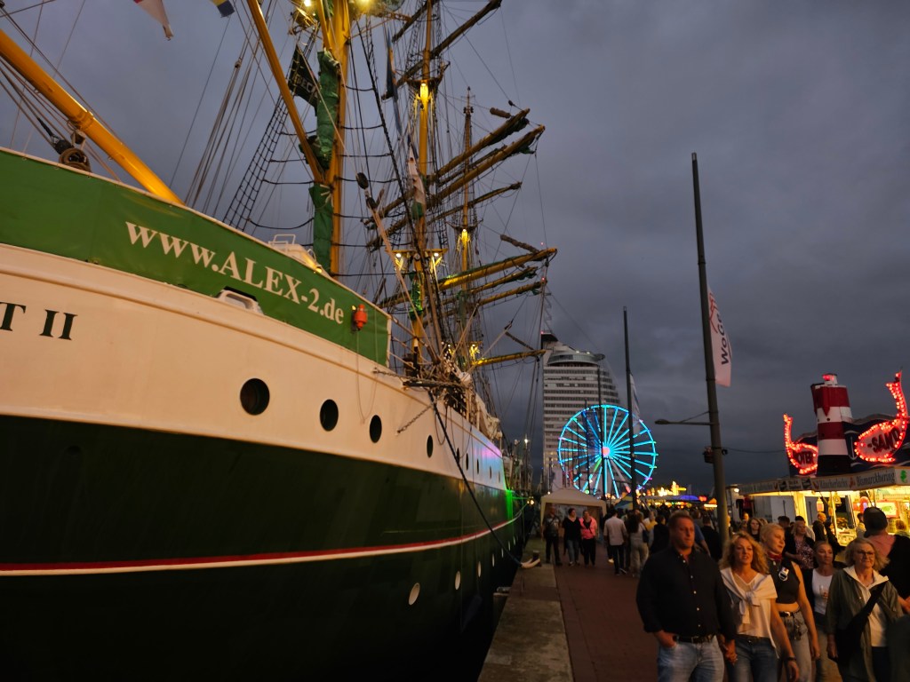 Nächtliche Aussicht auf das Segelschiff Alexander von Humboldt II im Hafen von Bremerhaven, mit beleuchtetem Riesenrad und festlicher Atmosphäre in der Umgebung.