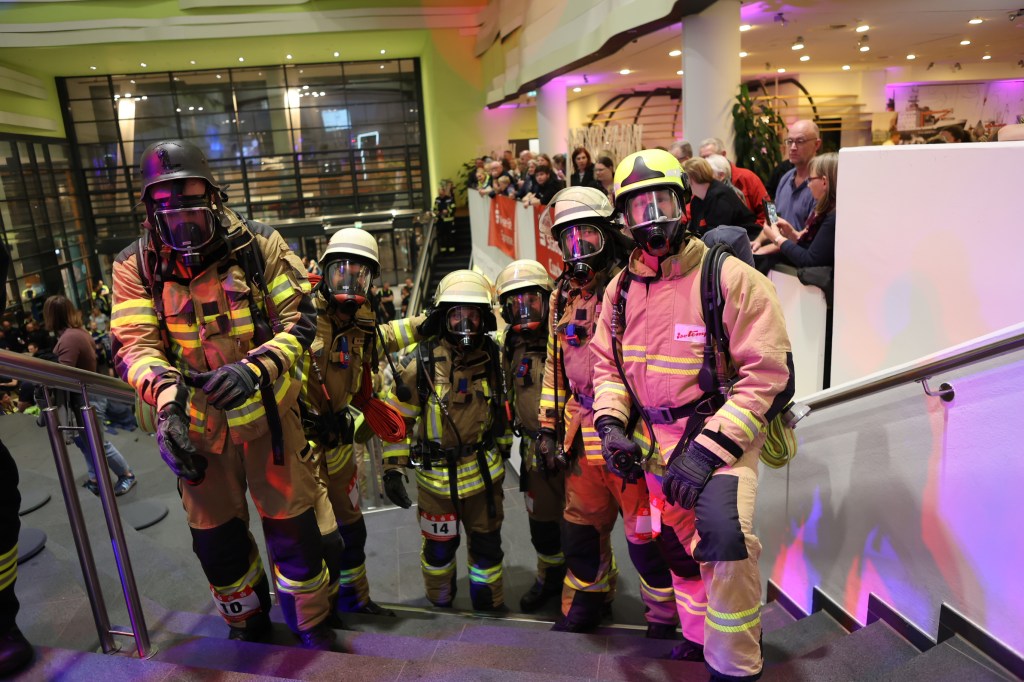 Gruppe von Feuerwehrleuten in Einsatzmontur mit Atemschutzanlagen, die auf einer Treppe stehen und sich auf einen Wettlauf vorbereiten.