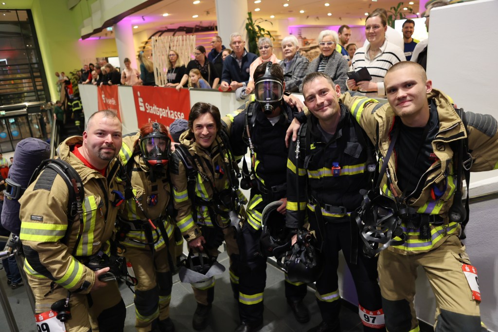 Gruppenfoto von fünf Einsatzkräften in Feuerwehrmontur beim Blaulichtlauf im Klimahaus Bremerhaven, umgeben von Zuschauern.