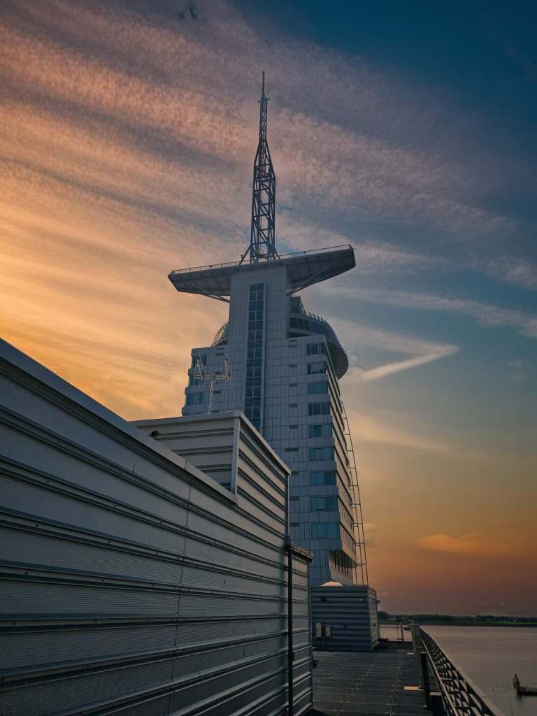 Blick auf das Atlantic Hotel Sail City in Bremerhaven bei Sonnenuntergang, mit eleganter Architektur und einem markanten Turm.