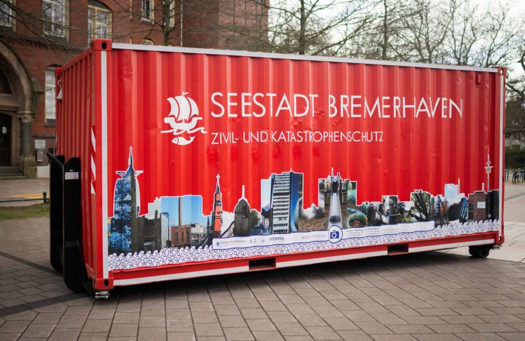 A red shipping container featuring the text 'Seestadt Bremerhaven Zivil- und Katastrophenschutz,' with various city landmarks illustrated along the bottom.