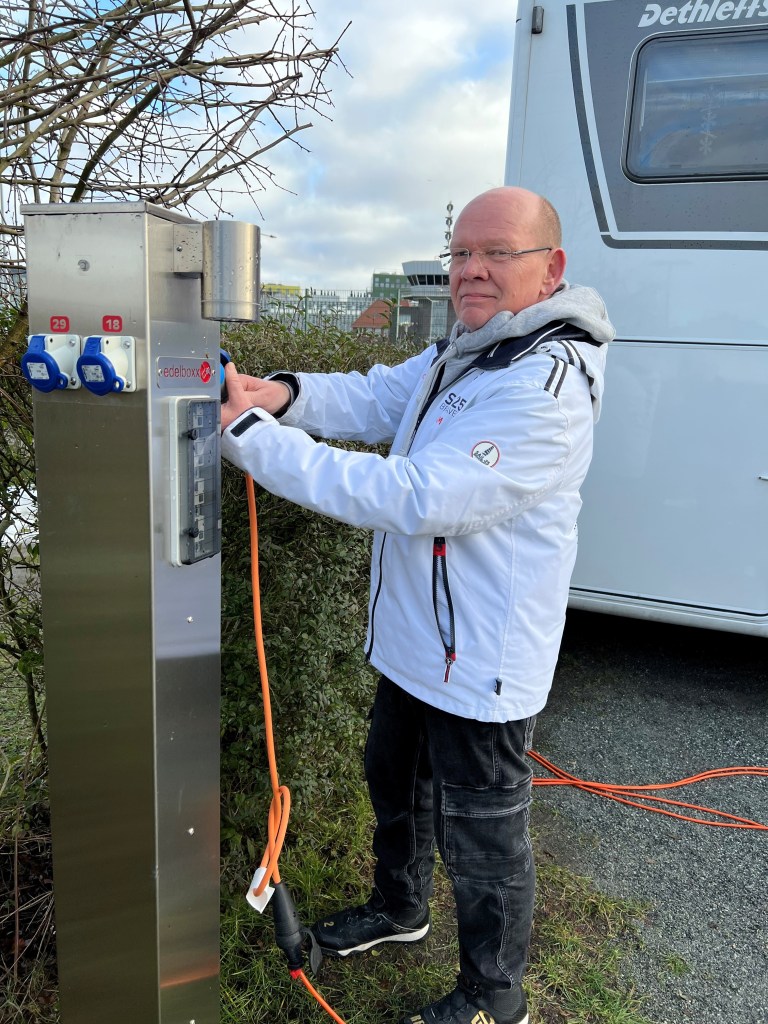Eine Person, die an einer Stromtankstelle für Wohnmobile steht und ein Kabel anschließt.