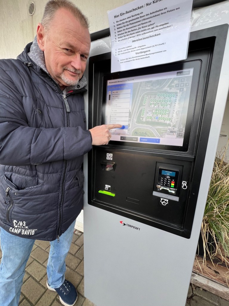 Mann zeigt auf einen Bildschirm eines Ticketautomaten mit Anweisungen für das Ein- und Auschecken.