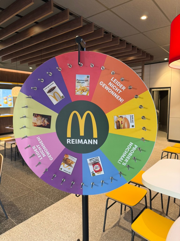 Ein bunten Glücksrad in einem McDonald's Restaurant mit verschiedenen Gewinnmöglichkeiten und dem Schriftzug 'Reimann'.