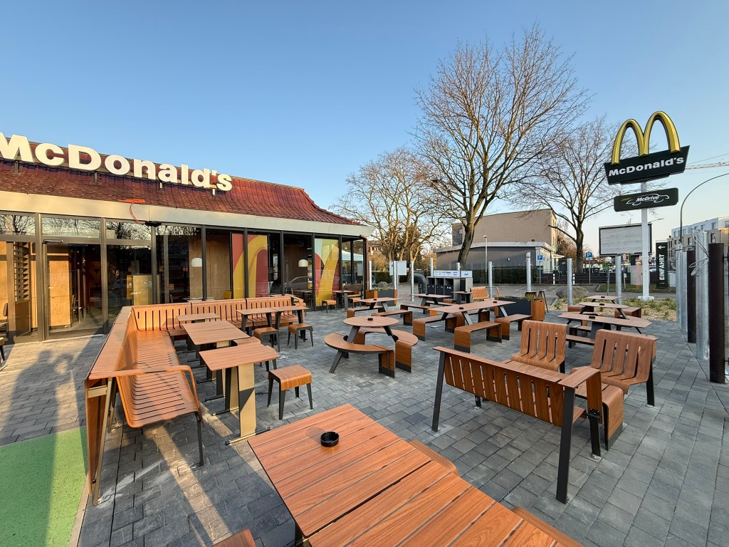 Außenansicht eines McDonald's Restaurants mit zahlreichen Tischen und Bänken im Freien.